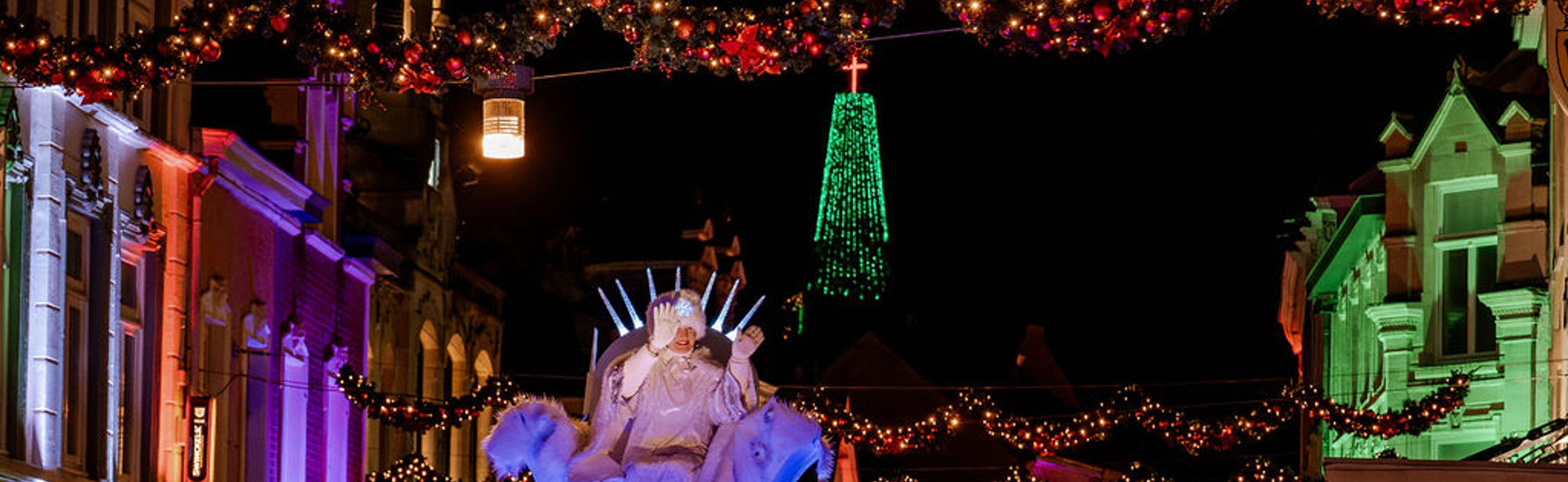 Vrouw met witte bontmuts zit op praalwagen in een met kerstlampjes versierde straat in Valkenburg