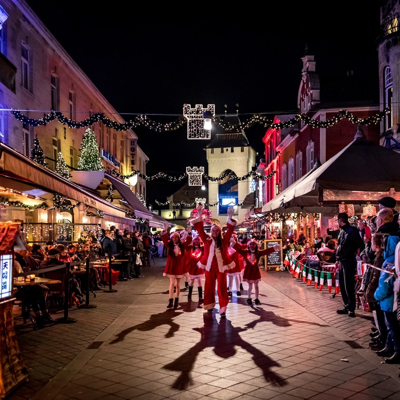 Groep kerstmeisjes dansend door de straten van Valkenburg terwijl publiek naar hen kijkt.