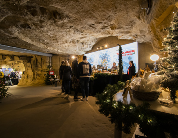 Mensen staan bij een kertstkraampje in een mergelgrot met daarachter een grote stadsplattegrond van valkenburg