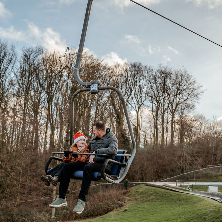 Vader en kind met kerstmuts zitten in de kabelbaan met op de achtergrond de Wilhelminatoren